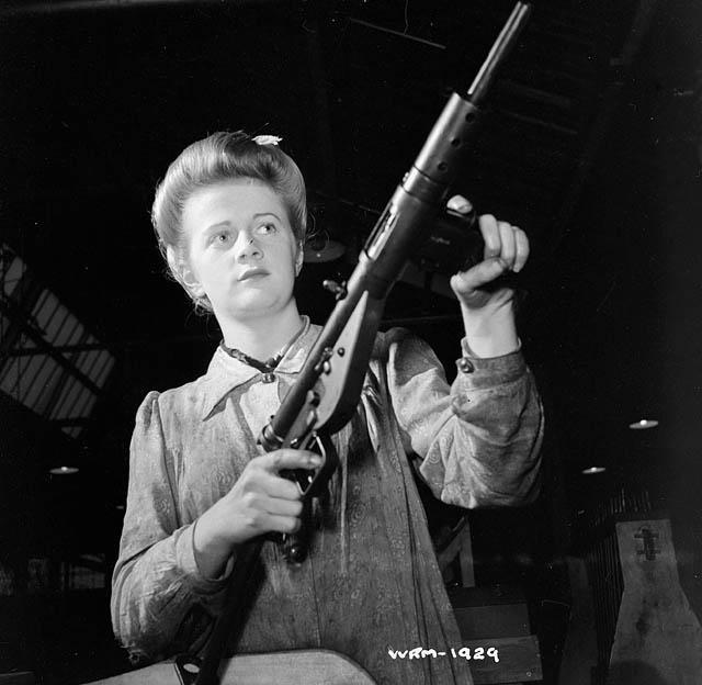 A worker holding a finished Sten Gun in a factory